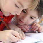 Two children drawing together, their heads close and eyes focused